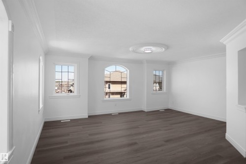 Spacious interior featuring wood-finish flooring, white walls, multiple windows including an arched window, and decorative crown molding - 6823 18 Avenue Sw, Edmonton, AB - Indoor Photo Showing Other Room
