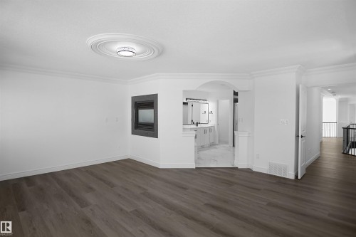 Wood-finish flooring, built-in fireplace, detailed crown molding, decorative ceiling medallion with attached lighting, and an arched entry - 6823 18 Avenue Sw, Edmonton, AB - Indoor Photo Showing Other Room