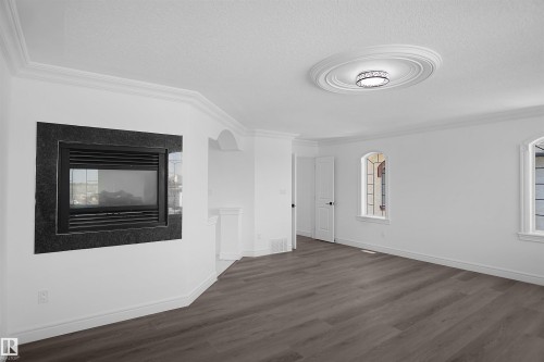 Recessed fireplace with a dark stone surround, crown molding, a decorative ceiling medallion, flush-mount lighting, and wood-finish flooring - 6823 18 Avenue Sw, Edmonton, AB - Indoor With Fireplace