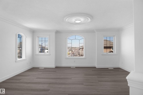 Spacious room featuring wood-finish flooring, a decorative ceiling medallion with an attached light fixture, crown molding, and multiple windows including an arched window - 6823 18 Avenue Sw, Edmonton, AB - Indoor Photo Showing Other Room