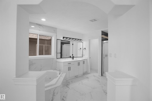 White cabinetry with black hardware, double vanity with integrated sinks, large framed mirror, recessed lighting, and a built-in corner bathtub - 6823 18 Avenue Sw, Edmonton, AB - Indoor