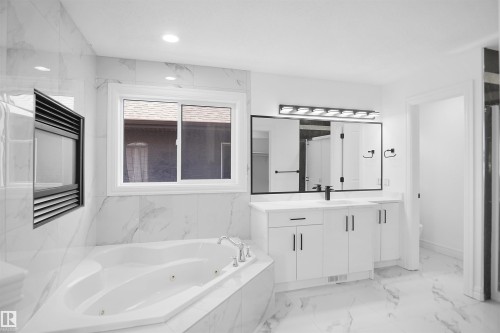 Corner soaking tub, built-in wall fireplace, marble-look tile flooring, dual-sink vanity with white cabinetry, and a large wall mirror with integrated lighting - 6823 18 Avenue Sw, Edmonton, AB - Indoor Photo Showing Bathroom
