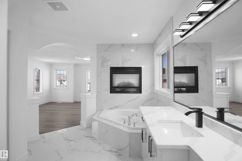 Soaking tub with tile surround, built-in fireplace, vanity with integrated sink, matte black faucet, and large mirror with integrated lighting - 6823 18 Avenue Sw, Edmonton, AB - Indoor Photo Showing Other Room With Fireplace