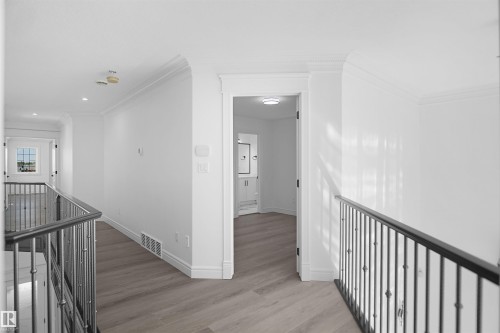 Bright hallway with wood-finish flooring, white walls, and metal railings - 6823 18 Avenue Sw, Edmonton, AB - Indoor Photo Showing Other Room