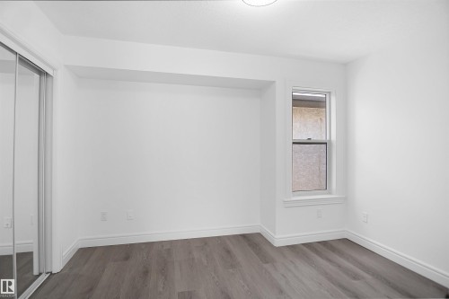 Recessed wall alcove, wood-finish flooring, single window, mirrored closet doors, and a flush-mount ceiling light fixture - 6823 18 Avenue Sw, Edmonton, AB - Indoor Photo Showing Other Room