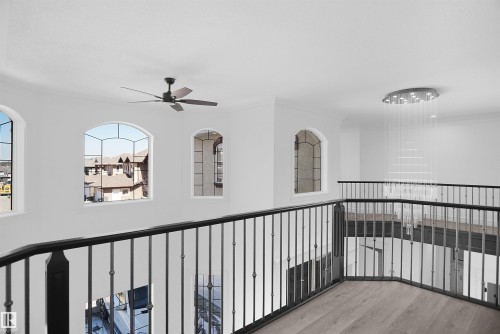 Open loft area featuring arched windows, a modern multi-tier chandelier, a ceiling fan, and wrought iron railings - 6823 18 Avenue Sw, Edmonton, AB - Indoor Photo Showing Other Room