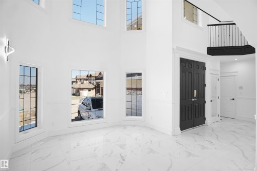 Two-story foyer featuring a double-height ceiling, large grid-pattern windows, marble-pattern flooring, and a dark double entry door with gold-tone hardware - 6823 18 Avenue Sw, Edmonton, AB -  Photo Showing Other Room