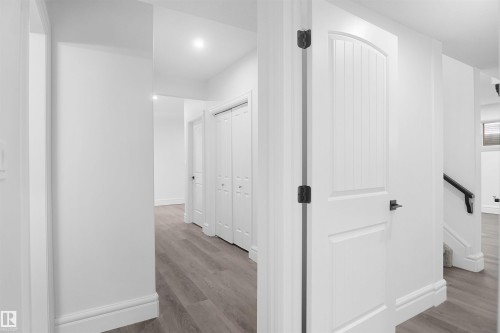 Hallway featuring wood-finish flooring, recessed lighting, white doors, and a black handrail - 6823 18 Avenue Sw, Edmonton, AB - Indoor Photo Showing Other Room