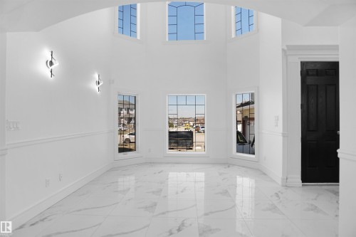 Two-story entry featuring arched windows, multiple fixed-pane windows, decorative wall sconces, and large format marble-look tile flooring - 6823 18 Avenue Sw, Edmonton, AB - Indoor Photo Showing Other Room
