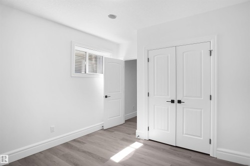 White interior walls, wood-finish flooring, white window with blinds, white paneled bifold doors with black hardware, white paneled door with black hardware, recessed ceiling lighting - 6823 18 Avenue Sw, Edmonton, AB - Indoor Photo Showing Other Room