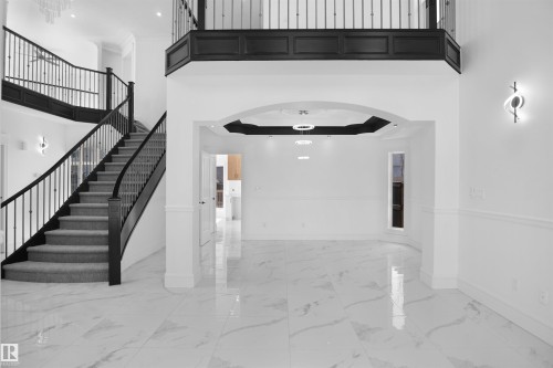 Grand curved staircase with wrought iron balusters, polished tile flooring, double-height ceiling, decorative wall sconces, and recessed lighting - 6823 18 Avenue Sw, Edmonton, AB - Indoor Photo Showing Other Room