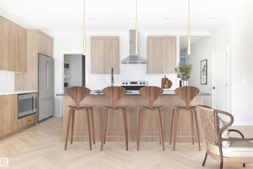Gourmet kitchen with wood-finish cabinetry, stainless steel appliances, a kitchen island with seating, and light wood-finish flooring in a herringbone pattern - 24 Clichy Close, St. Albert, AB - Indoor Photo Showing Kitchen With Upgraded Kitchen