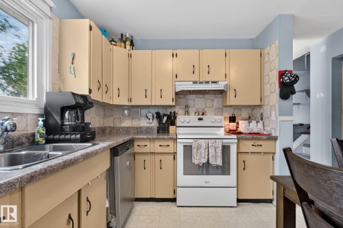 Kitchen featuring ample cabinetry, a double basin stainless steel sink, a built-in dishwasher, and a white electric range - 8031 27 Avenue Nw, Edmonton, AB - Indoor Photo Showing Kitchen With Double Sink