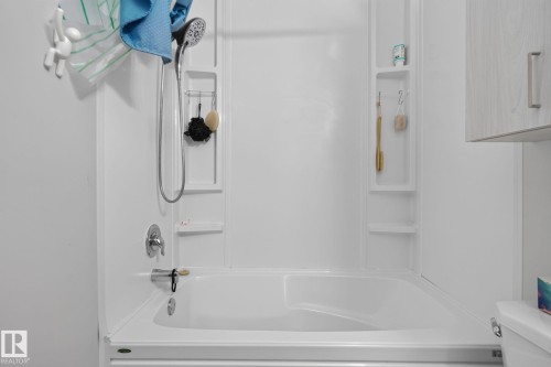 White bathtub and shower combination with an integrated multi-level shelving system, chrome fixtures, and a handheld showerhead - 8031 27 Avenue Nw, Edmonton, AB - Indoor Photo Showing Bathroom