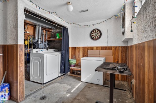 Laundry area featuring a side-by-side washer and dryer, wood-panel wall accents, and a textured wall finish - 8031 27 Avenue Nw, Edmonton, AB - Indoor Photo Showing Laundry Room