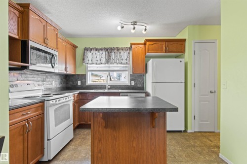 Kitchen featuring wood-finish cabinetry, a built-in microwave, a tile backsplash, and a central island with countertop - 9118 Scott Crescent Nw, Edmonton, AB - Indoor Photo Showing Kitchen