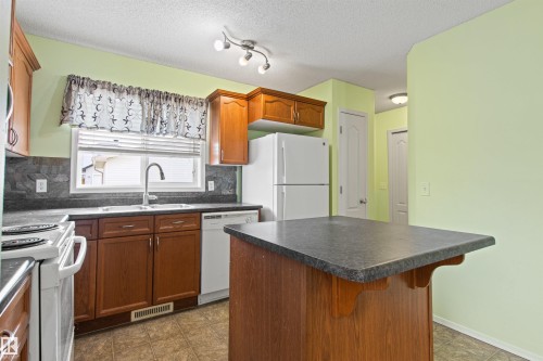 Kitchen featuring wood cabinetry, a center island with a dark countertop, white appliances, and a double basin sink with a gooseneck faucet - 9118 Scott Crescent Nw, Edmonton, AB - Indoor Photo Showing Kitchen
