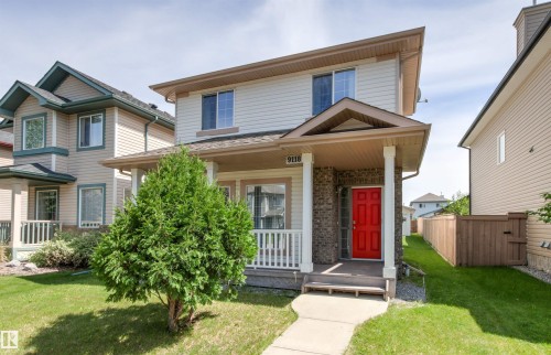 Two-story home with a covered front porch featuring white pillars, brick accents, and a vibrant red entry door - 9118 Scott Crescent Nw, Edmonton, AB - Outdoor With Deck Patio Veranda