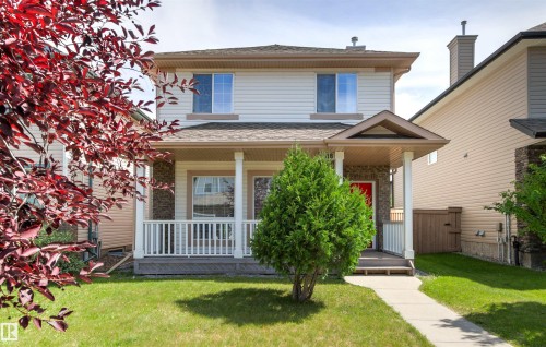 Two-story residence featuring light-colored siding, a covered front porch with white railings, a red front door, and a concrete pathway leading to the entrance - 9118 Scott Crescent Nw, Edmonton, AB - Outdoor With Deck Patio Veranda