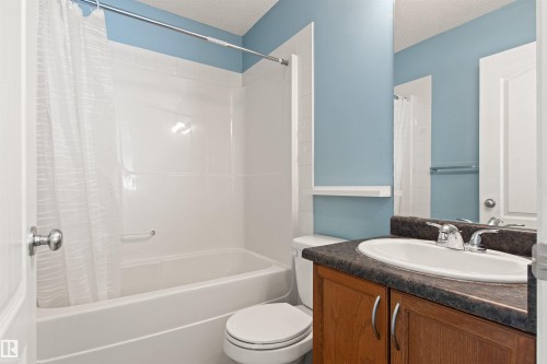 Built-in bathtub with integrated shower, white paneled surround, wood-finish vanity with a dark countertop, and an oval undermount sink with chrome fixtures - 9118 Scott Crescent Nw, Edmonton, AB - Indoor Photo Showing Bathroom