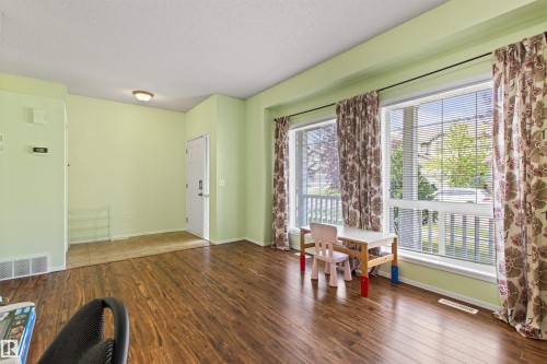 Wood-finish flooring throughout, bright window light, and a white entry door - 9118 Scott Crescent Nw, Edmonton, AB - Indoor Photo Showing Other Room