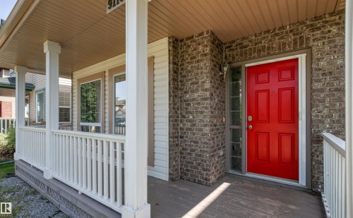 Inviting covered front porch with white railing, light siding, brick accents, and a vibrant red entry door with sidelight - 9118 Scott Crescent Nw, Edmonton, AB - Outdoor With Exterior