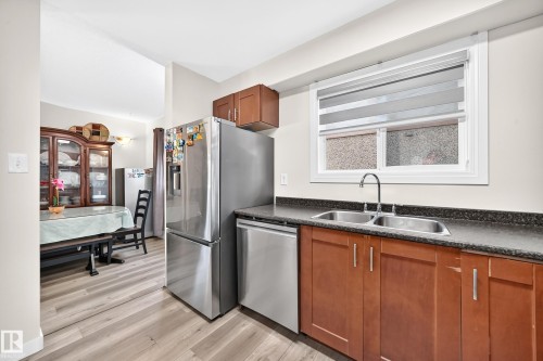 Kitchen featuring stainless steel appliances, dark countertops, wood-finish cabinetry, and a double basin sink - #22 3812 20 Av Nw, Edmonton, AB - Indoor Photo Showing Kitchen With Double Sink