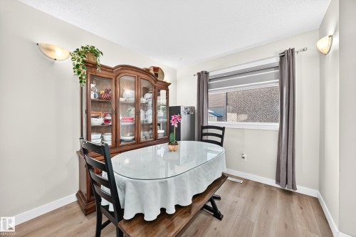 Wood-finish flooring, wall-mounted sconce lighting, and window with privacy blind - #22 3812 20 Av Nw, Edmonton, AB - Indoor Photo Showing Dining Room