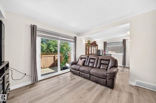 Wood-finish flooring throughout, sliding glass door, and a built-in wall niche with sconce lighting - #22 3812 20 Av Nw, Edmonton, AB - Indoor Photo Showing Living Room
