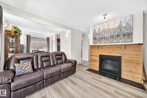 Wood-finish flooring, fireplace with wood paneling and dark tile hearth, recessed lighting, and wall sconces - #22 3812 20 Av Nw, Edmonton, AB - Indoor Photo Showing Living Room With Fireplace