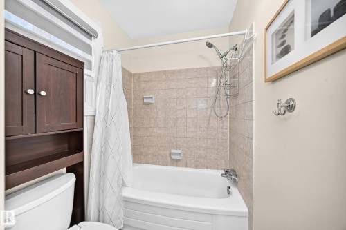 White bathtub with tiled surround, showerhead with handheld attachment, and an over-toilet storage cabinet - #22 3812 20 Av Nw, Edmonton, AB - Indoor Photo Showing Bathroom