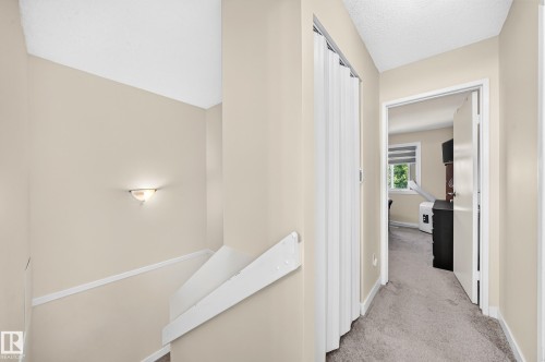 Wall-mounted sconce lighting, neutral wall palette, carpeted hallway, bi-fold closet doors, and painted stair railing - #22 3812 20 Av Nw, Edmonton, AB - Indoor Photo Showing Other Room