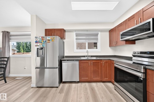 Kitchen featuring wood-finish flooring, stainless steel appliances, dark countertops, and wood cabinetry - #22 3812 20 Av Nw, Edmonton, AB - Indoor Photo Showing Kitchen With Double Sink