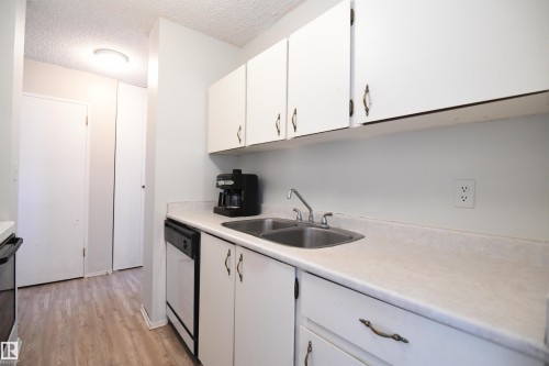 The kitchen is a simple, white, galley design, but is open at both ends, maximizing flow, and keeping the open feel - #1305 13910 Stony Plain Rd Nw, Edmonton, AB - Indoor Photo Showing Kitchen With Double Sink