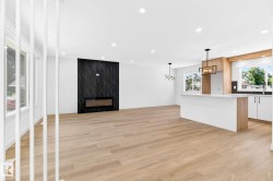 Bright interior with wood-finish flooring, a modern fireplace with a dark patterned surround, a kitchen island with a white countertop, and contemporary pendant lighting fixtures - 