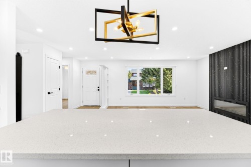 White quartz countertop, modern chandelier, recessed lighting, wood-finish flooring, and a black accent wall with a linear fireplace - 5 Peace River Drive, Devon, AB - Indoor