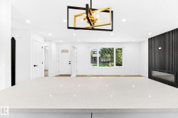 White quartz countertop, modern chandelier, recessed lighting, wood-finish flooring, and a black accent wall with a linear fireplace - 