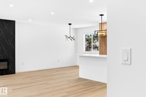 White walls with recessed lighting, wood-finish flooring, a modern black fireplace surround, a built-in kitchen island, and contemporary pendant lighting - 5 Peace River Drive, Devon, AB - Indoor Photo Showing Other Room