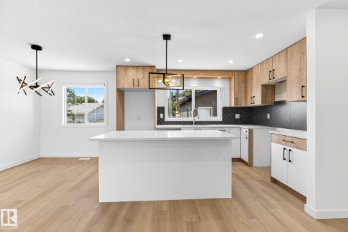Kitchen featuring a white island with a light-colored countertop, wood-finish cabinetry, white lower cabinetry, black herringbone pattern backsplash, and wood-finish flooring - 5 Peace River Drive, Devon, AB - Indoor Photo Showing Kitchen