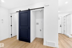 Laundry area featuring a dark panel barn door on a black track and wood-finish flooring - 