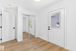 Wood-finish flooring, white walls, white doors with black hardware, mirrored closet doors, and recessed lighting - 