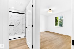 Bathroom featuring a shower with glass enclosure, marble-style tile surround, and matte black fixtures - 