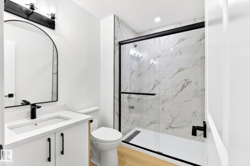 Contemporary bathroom featuring a white vanity with black hardware, an arched mirror, and a walk-in shower with a glass enclosure - 5 Peace River Drive, Devon, AB - Indoor Photo Showing Bathroom