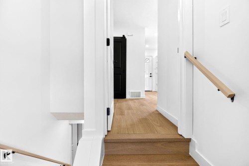 Hardwood flooring throughout, white walls, black interior door, wood handrail with black brackets, and white trim - 5 Peace River Drive, Devon, AB - Indoor Photo Showing Other Room