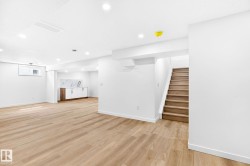 Spacious open-concept room featuring wood-finish flooring, recessed lighting, and a built-in wet bar with white cabinetry and a patterned backsplash - 
