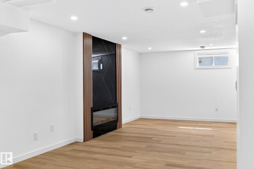 Integrated electric fireplace with a dark-toned surround, wood-finish accent paneling, recessed ceiling lighting, and wood-finish flooring - 5 Peace River Drive, Devon, AB - Indoor Photo Showing Other Room