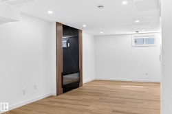 Integrated electric fireplace with a dark-toned surround, wood-finish accent paneling, recessed ceiling lighting, and wood-finish flooring - 