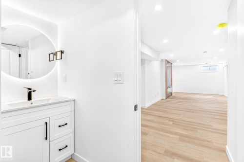 White vanity with black hardware, round illuminated mirror, and a black-finish faucet - 5 Peace River Drive, Devon, AB - Indoor
