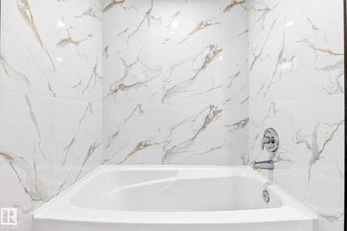 Built-in bathtub with a white finish, surrounded by large format wall tile with a veined pattern, and polished chrome fixtures - 5 Peace River Drive, Devon, AB - Indoor Photo Showing Bathroom