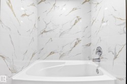 Built-in bathtub with a white finish, surrounded by large format wall tile with a veined pattern, and polished chrome fixtures - 